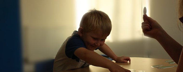 A young boy reaching across a table of picture cards while Sarah holds another card up for him