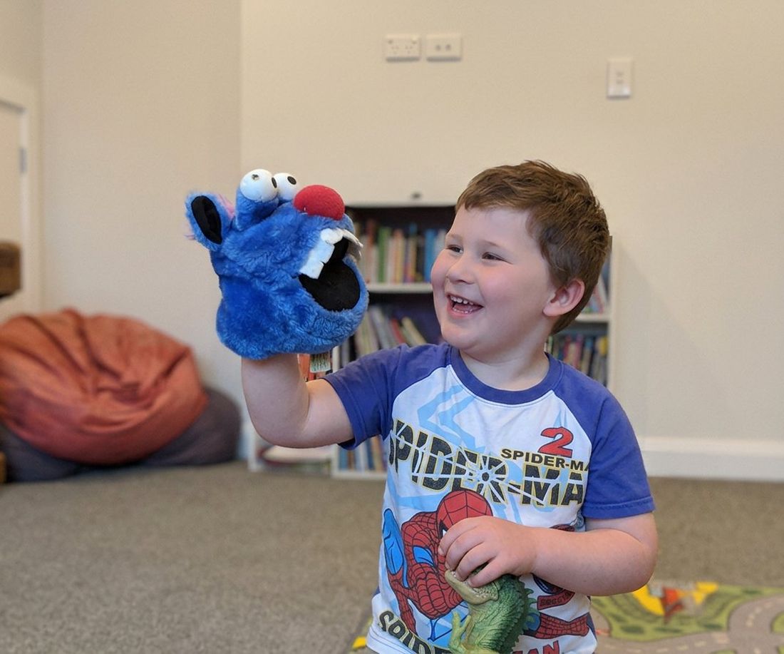 A preschooler laughing while playing with a hand puppet in the therapy room